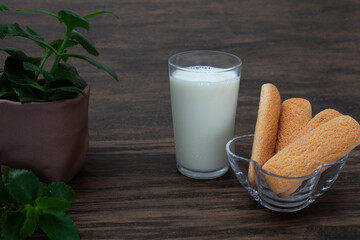 Brazilian champagne biscuit in focus ahead with glass of milk and vase with green leaves slightly defocused on wooden background.