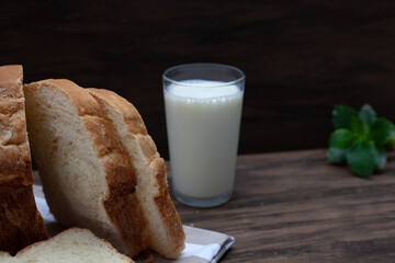 Homemade bread in focus ahead with glass of milk and slightly blurred green leaves in the background. Wood background.