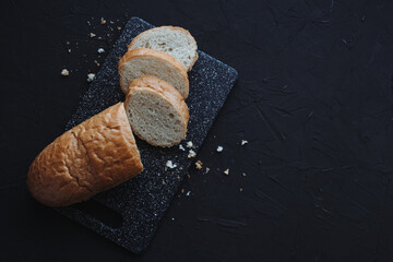 Sliced baguette on black background. Fresh homemade baked bread. Top view with copy space.