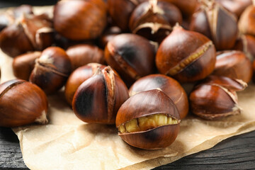 Tasty roasted edible chestnuts on black wooden table, closeup