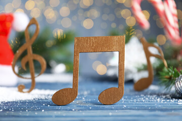 Wooden music note on light blue table against blurred Christmas lights