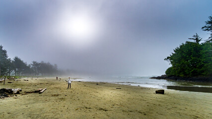 People walking on the Sandy Beach of Cox Bay in Dense Fog hanging over the Beach and Pacific Ocean at the Pacific Rim National Park on Vancouver Island, British Columbia, Canada