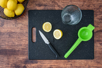 Fresh lemon halves on a black cutting board, paring knife, wood table, basket of lemons, citrus...