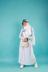 Fashion photo of a beautiful elegant young asian woman holding handbag posing over blue background.