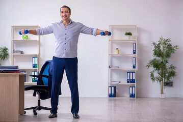 Young handsome male employee doing exercises in the office