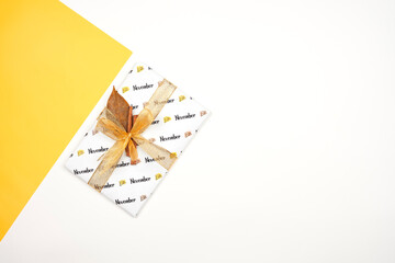 Thanksgiving day present. Bright gift tied with ribbon and cinnamon. November gift box on bright yellow and white split background