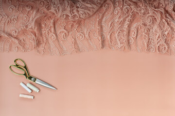 Obraz premium Top view of pink coral coloured lace and silk fabric with tailoring accessories near cup of coffee