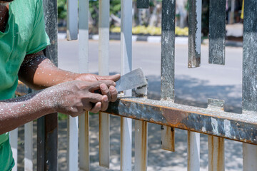 Hands of worker use a putty to strip paint of fence