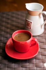 Red cup of coffee next to a milk pot.