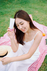 Asian traveler woman in white dress with white lotion bottle at park outdoors.