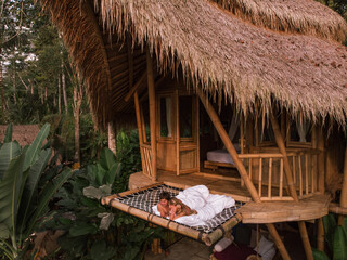 Young caucasian travel couple lie on hammock in bamboo eco house, nature and mountains on background. Couple wake up in outdoor jungle bed