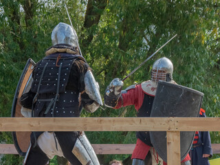 Tver / Russia - September 29 2020: Warriors in heavy armor fight with swords. In the background,...