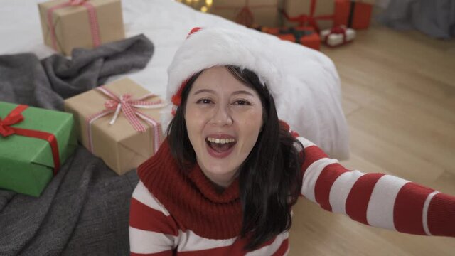 front view cheerful vlogger waving hi to the camera is showing and introducing the gift she got while live streaming online on Christmas day at home.