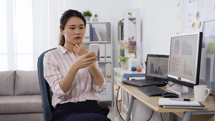 elegant asian office lady worker is working from home and replying message on mobile phone in the morning.