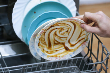 A man loads dirty dishes, plates, spoons, forks, cutlery into dishwasher tray.