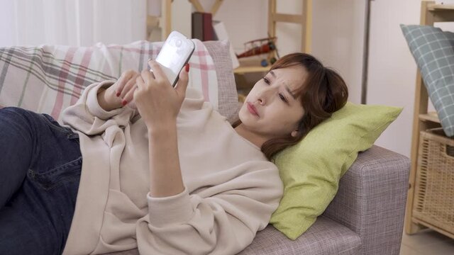 yawning unemployed woman reclining on couch throwing her phone on floor after making sure not getting any notification, looking away unhappily.