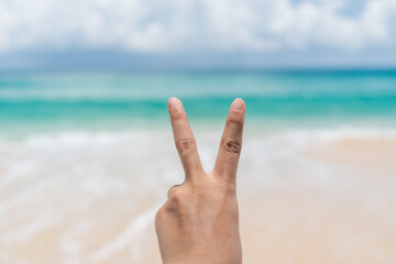 Woman hand do peace out with blue sky beach.