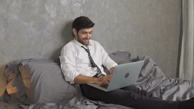 Footage B roll of Manager man in suit being in business trip lying on bed in hotel room and speaking online using laptop. Startup business concept. Business relaxing concept.