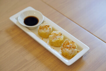 Dim Sum Recipe - Chinese shrimp dumplings topped with fried garlic, served with sour sauce on white plate.