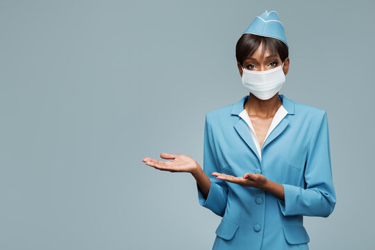 Young african stewardess wearing an antiviral mask on her face. Boarding gesture.