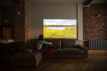 Woman imitates a walk in mountains while looking at projector during quarantine while sitting at...
