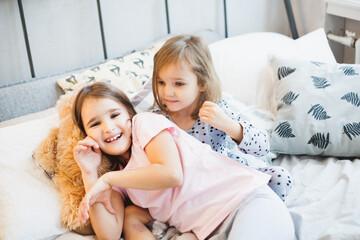 The room is decorated for the new year, the little sisters are sitting on the bed, playing games, pillows, laughing, waiting for Christmas