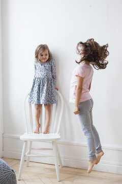 Girls Sisters Near A White Wall And A Chair, Height Measurement, Games, Who Is Taller, Laughter, Arguments, Emotions