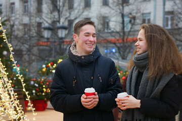 Young boy and girl are having fun outdoor at Christmas market. Cute couple spends time together at the Christmas market drinking hot drinks. Date at Christmas Eve