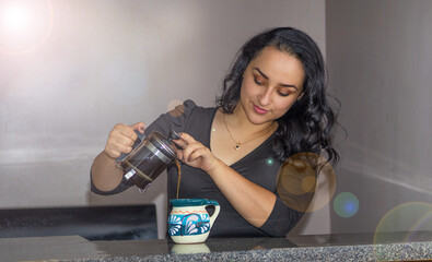 beautiful Mexican woman serving coffee from a French press to Mexican cup
