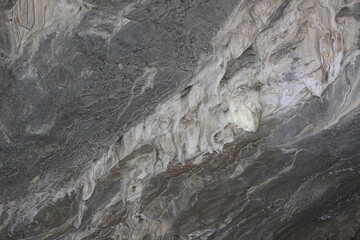 Naklejka premium View in a dark cave with gray walls. The surface of the stone wall of the cave. Gray ancient stone texture background. Beautiful gray stalactites in the cave. Russia, South Ural, Bashkortostan