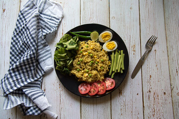 Noodles, vegetables and slices of egg condiments on a black plate.