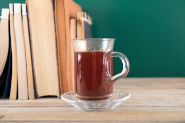 A pile of textbooks in front of the blackboard and a cup of coffee next to the books