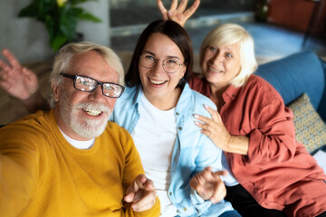 Cheerful grandfather, grandmother and granddaughter take a selfie and make faces at home