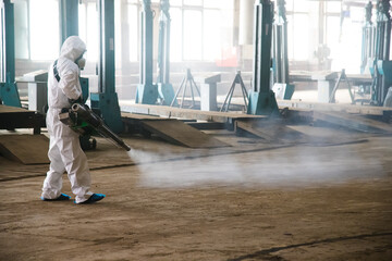 Worker in a protective suit handles industrial premises, buildings, and interiors to protect...