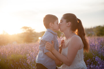 love concept young mother kissing happy child on summer nature flower field