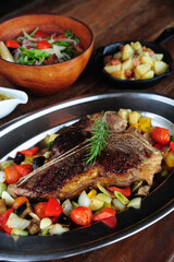 Grilled beef steak with rosemary, salt and pepper on black stone plate. Grilled striploin sliced steak. Juicy thick grilled beef steak seasoned with rosemary fresh of the summer BBQ.