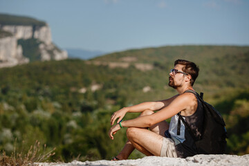 Naklejka na ściany i meble Young male hiker with backpack relaxing on top of a mountain during calm summer sunset