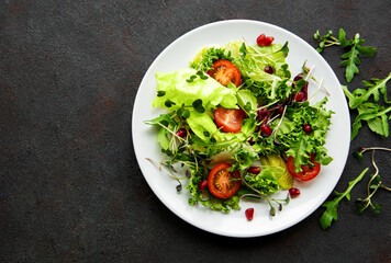 Fresh green mixed  salad bowl with tomatoes and microgreens  on black concrete background. Healthy food, top view.