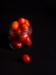 low key photo of cherry tomatoes in a glass jar isolated on black background
