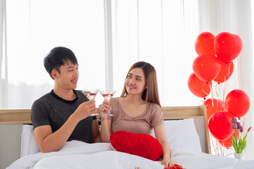 A happy young couple is raising a glass of wine to cheer in the bed on their bedroom. Couple lovers are giving a toast.