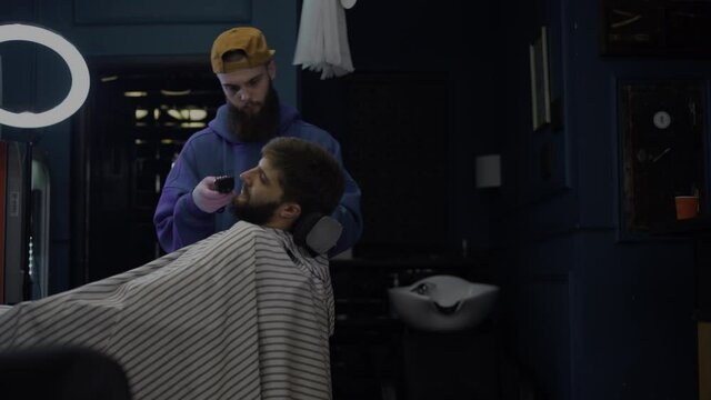 A bearded man trims his beard in a barber shop. Barber works as a trimer in a salon