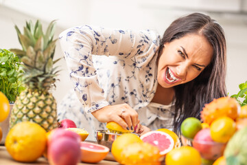 Woman squeezing an orange hard at home with plenty of fruit around her