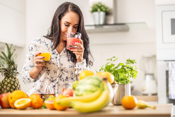 Woman smells freshly squeezed juice from a cup in a kitchen full of fruit