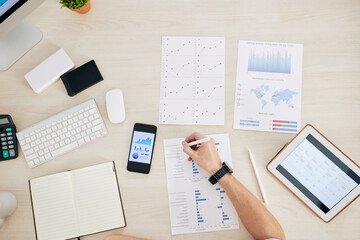 Entrepreneur analyzing documents with charts and reports at office table, view from the top