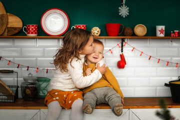Toddler with older sister children hugging in the new year's kitchen, the concept of cozy christmas...