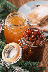 Closeup of a orange and dogwood jam jars on a wooden table with apple strudel on background