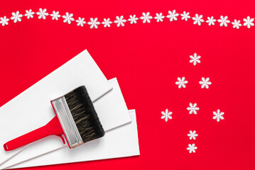 A large new red plastic paint brush in metal edging for painting and white wood planks and Christmas tree from snowflakes on a red background. Banner with copy space for a hardware store or art shop