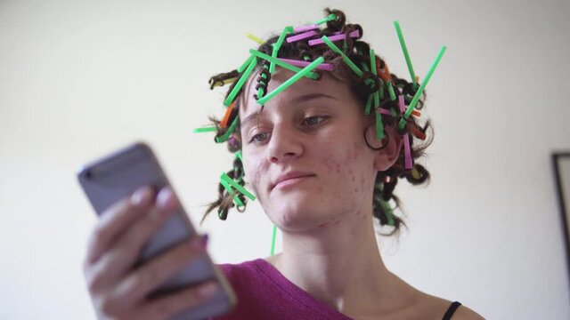 Curly hair teen making afro hairstyle with plastic straw using mobile phone