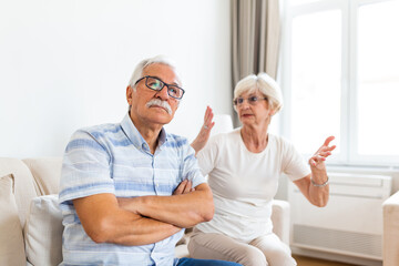 Angry elderly woman arguing with her husband. Senior couple having difficulty in marriage. Old couple sitting on the sofa at home