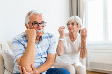 Senior couple arguing. Elderly woman frustrated with her husband. Older couple sitting on the sofa at home,having fight. Marriage issues, pre-divorce period